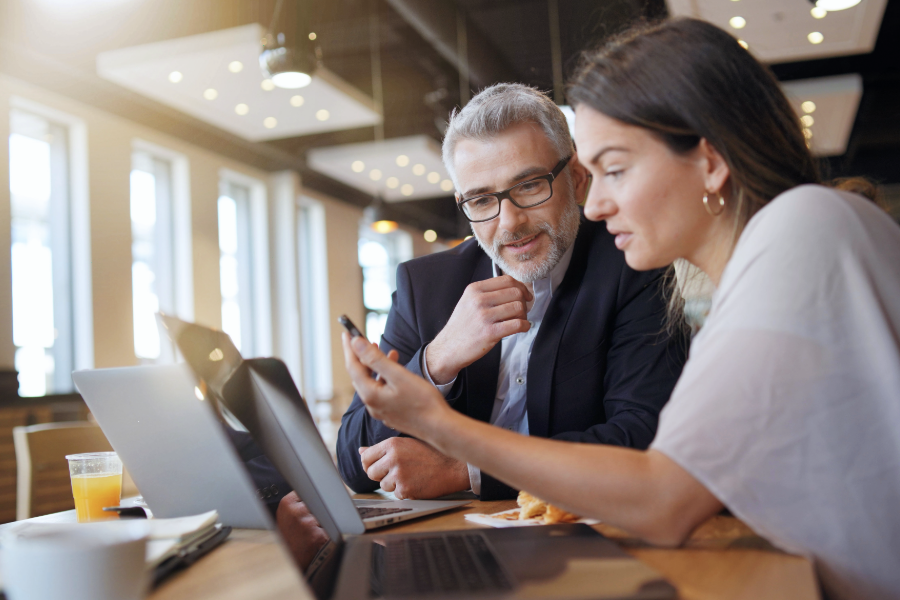 man and woman talking to someone on phone while sitting at table with laptops